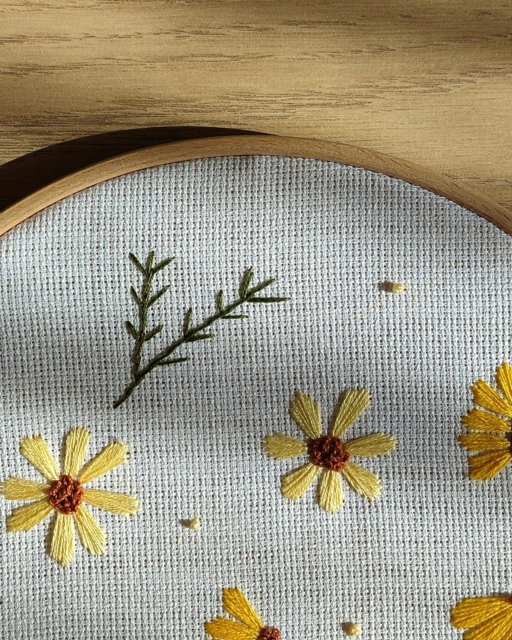 Beautiful embroidery of yellow flowers on canvas, framed in a wooden hoop with natural light.